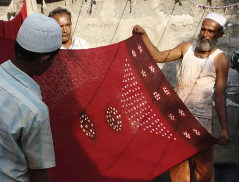 Khatri artisans holding up a red bandhani cloth with white tie-dyed dots