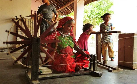 Woman spinning yarn on a wooden charkha in a weaver’s home at Bhujodi