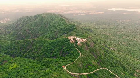 Aerial view of a green hill with a shrine on its slope and a winding road leading up to it