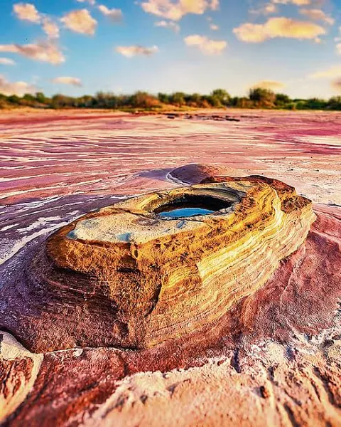 Layered rock with a small pool of rainwater on pink and white eroded ground at Jatavira