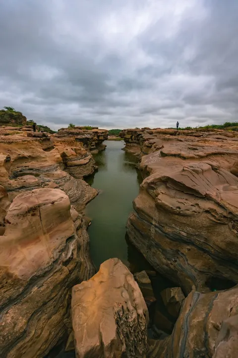 Water-filled channel between layered sandstone walls at Kadiya Dhro under monsoon clouds