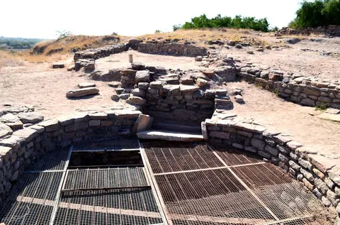 Excavated stone-lined well under a protective metal grille at Khirasara