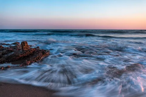 Waves washing over coastal rocks beside a small stone shrine at sunset