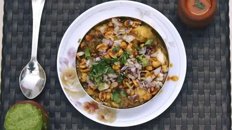 Bowl of Kutchi kadak topped with masala peanuts, onion and coriander, with green chutney beside it