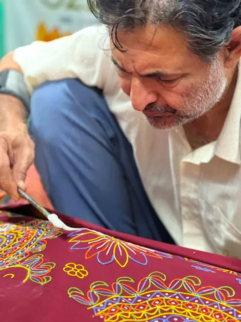 Rogan artist drawing oil paste onto maroon cloth